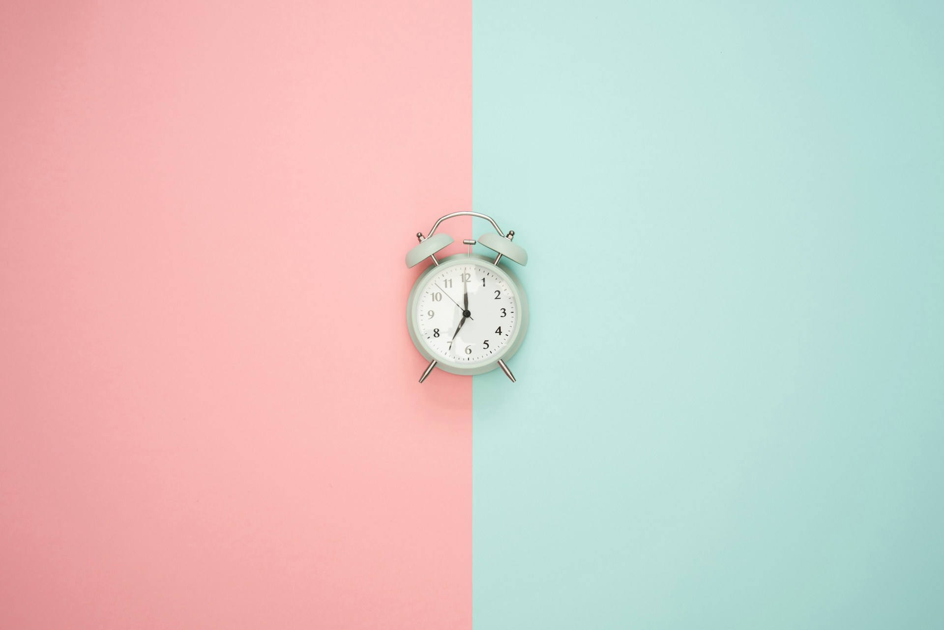 An alarm clock centred between a pink and a mint-green background.